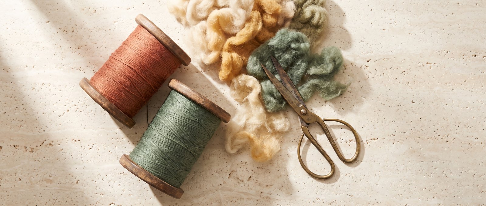 Raw materials: spools of terracotta and green silk thread, raw wool and brass tailoring shears